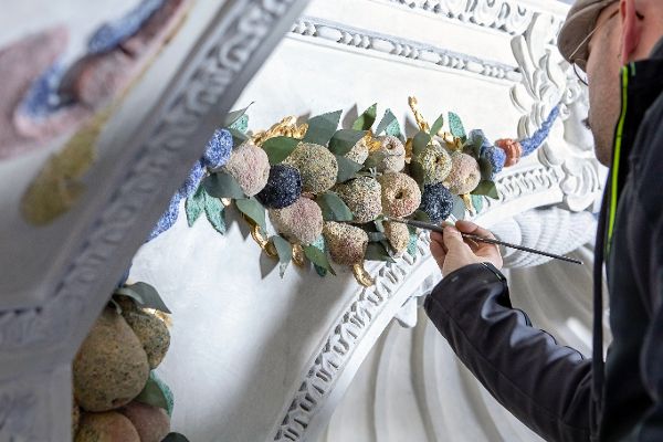 Ein Restaurator arbeitet mit Pinsel an einem Element aus Stuck, das einen Bund aus Früchten darstellt