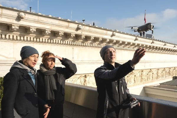ein Mann lässt auf dem Dach des Parlaments eine Drohnen in die Luft steigen, zwei Frauen sehen dabei zu