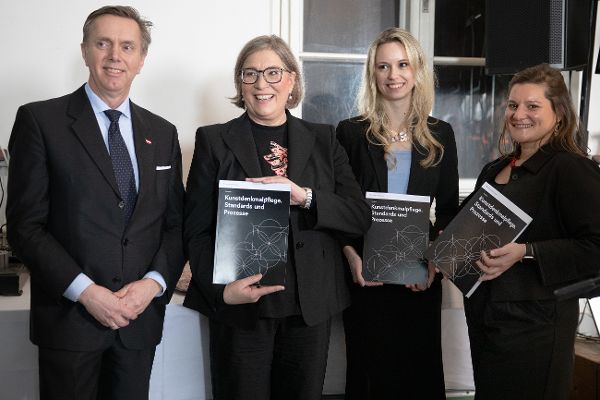 ein Man und drei Frauen stehen nebeneinander, die Frauen halten jeweils ein Exemplar der Publikation "Kunstdenkmalpflege. Standards und Prozesse" mit dem Cover in die Kamera