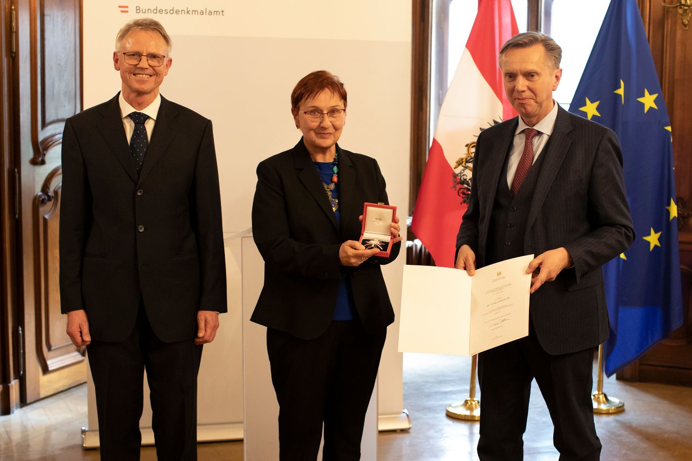 Drei Personen, eine Person hält eine Urkunde in der Hand