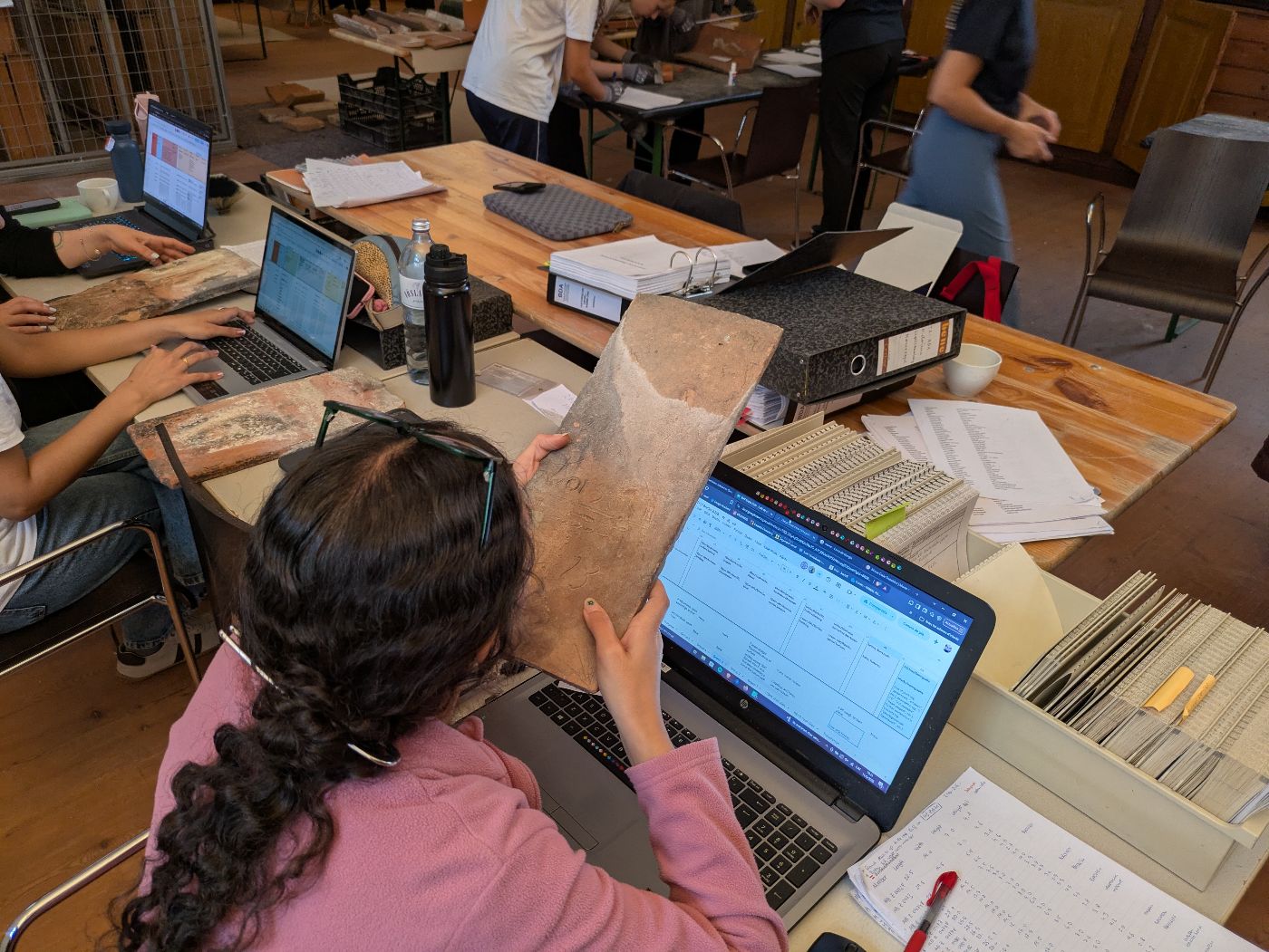 eine Gruppe von Studentinnen und Studenten untersucht historische Ziegel und gibt Daten in einen Computer ein