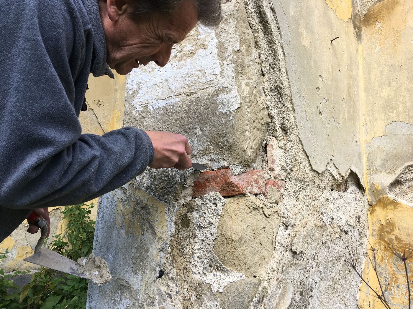 ein Mann arbeitet mit einer Spachtel an einer Ziegelmauer