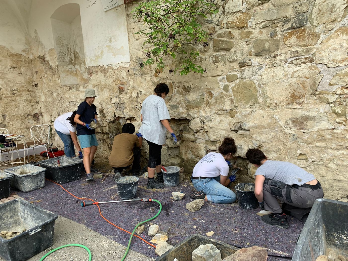 eine Gruppe junger Menschen arbeitet an einer historischen Mauer