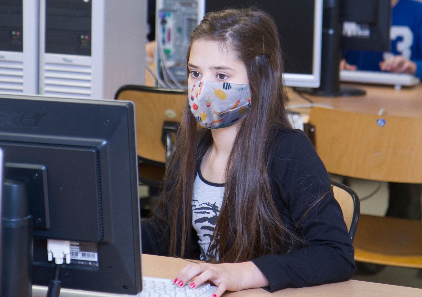 ein Mädchen trägt eine Maske und sitzt vor einem Computer