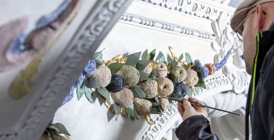 Ein Restaurator arbeitet mit Pinsel an einem Element aus Stuck, das einen Bund aus Früchten darstellt