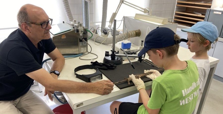 ein Mann erklärt zwei Kindern die Bedeutung ihres archäologischen Fundes