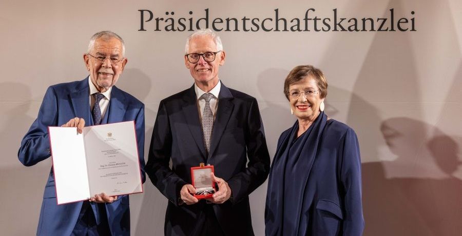 Christian Brugger hält die geöffnete Ordensschatulle, links von ihm hält Bundespräsident Alexander van der Bellen die dazugehörige Urkunde aufgeklappt in die Kamera, rechts von Christian Brugger steht Doris Schmidauer, die Ehefrau des Bundespräsidenten