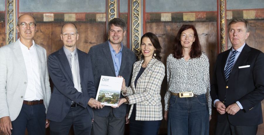 Gruppenfoto, ein Mann und eine Frau halten ein Buch gemeinsam in die Kamera