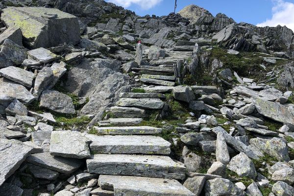 Zu Stufen geschlichtete große Steinplatten im steileren Gelände unterhalb der Passhöhe