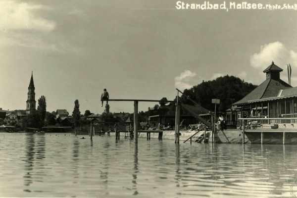 Schwarz-Weiß-Foto mit Blick vom Wasser auf den Steg und das Badehaus im Seebad in Mattsee