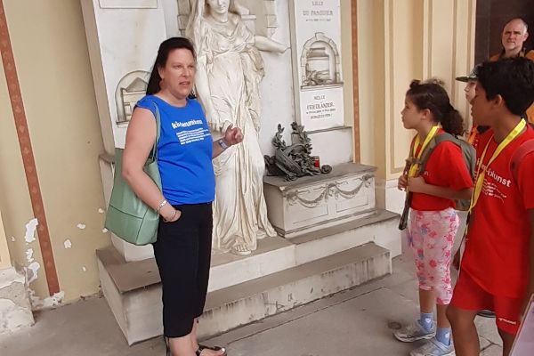Eine Frau erklärt Kindern eine Steinfigur auf einem Grabmal