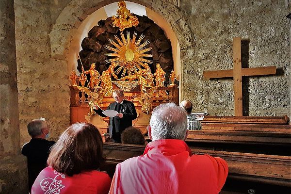 zwei Personen sitzen auf einer Kirchenbank, ein Priester predigt