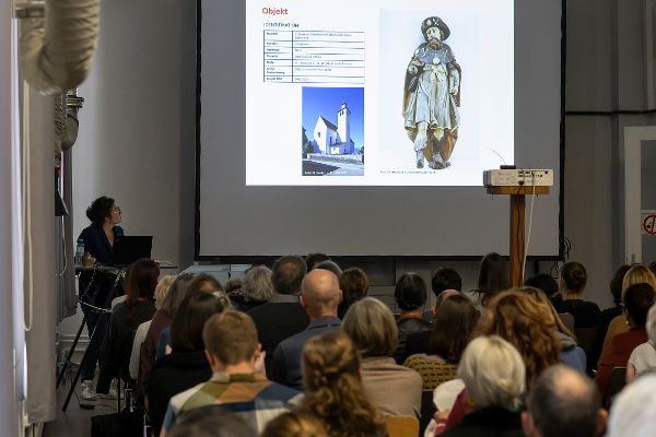 eine Frau redet, auf er der Wand sieht man eine Präsentation