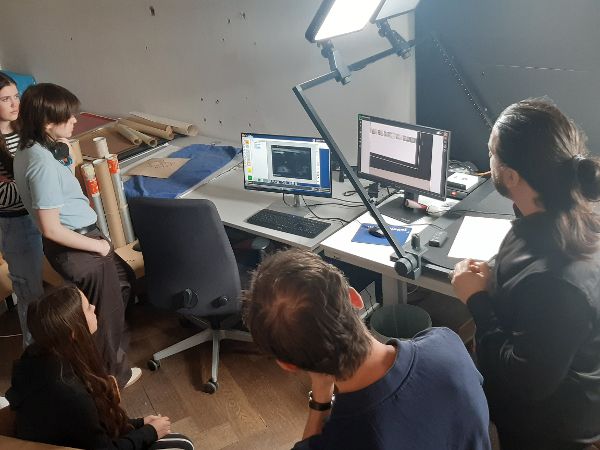 Kinder blicken gemeinsam mit Erwachsenen auf einen Bildschirm, daneben ist ein Scanner zu sehen
