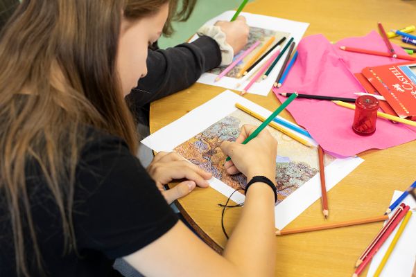 Blick über die Schulter eines Mädchens, das mit Buntstiften eine Zeichnung anfertigt