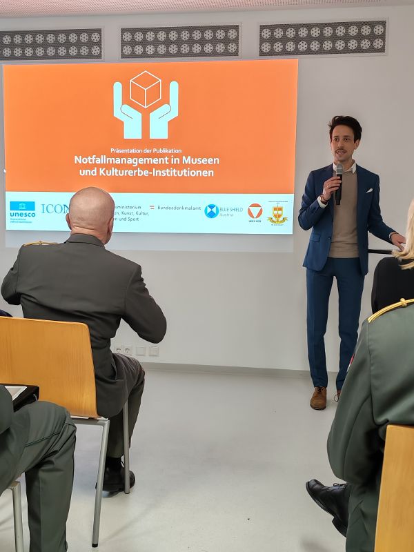 ein Mann steht in einem Vortragssaal vor einer Leinwand und spricht zu einem Publikum