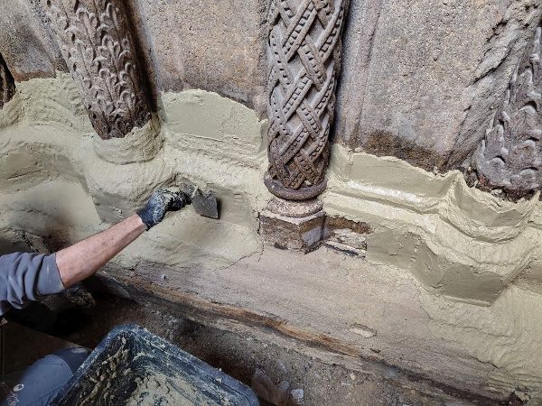 Ein Handwerker trägt mit einer Kelle eine Masse an einem Sockel aus Sandstein auf