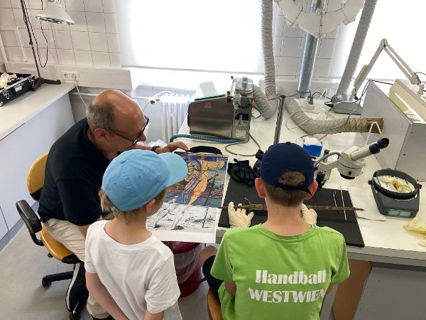 ein Mann erklärt zwei Kindern anhand eines Bildes wie die Soldaten der Schweizer Garde ausgerüstet waren