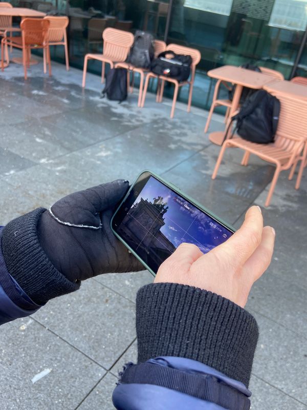 zwei Hände halten ein Handy, auf dem Display sieht man die aktuelle Bildaufnahme einer Drohne