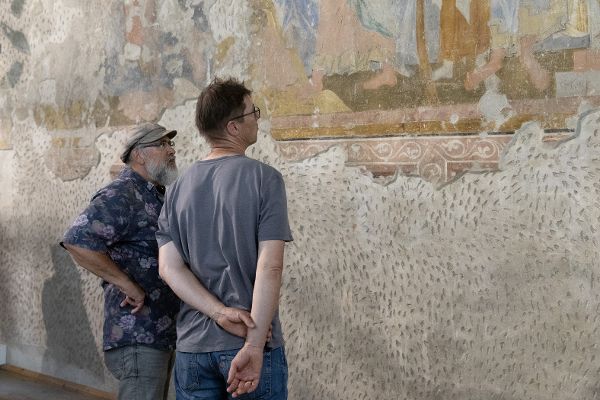 zwei Männer betrachten eine mittelalterliche Wandmalerei