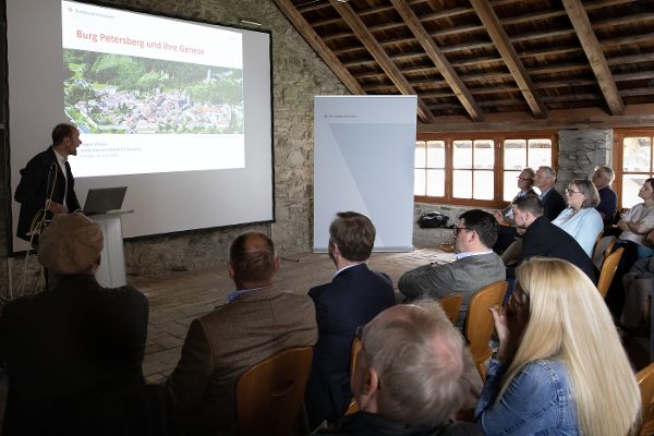 Votragassaal, ein Mann spricht von einem Rednerpult, dahinter eine Leinwand