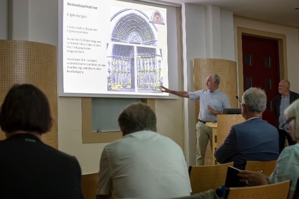 ein Mann steht vor einem mit Beamer an die Wand projizierten Foto und erklärt Details