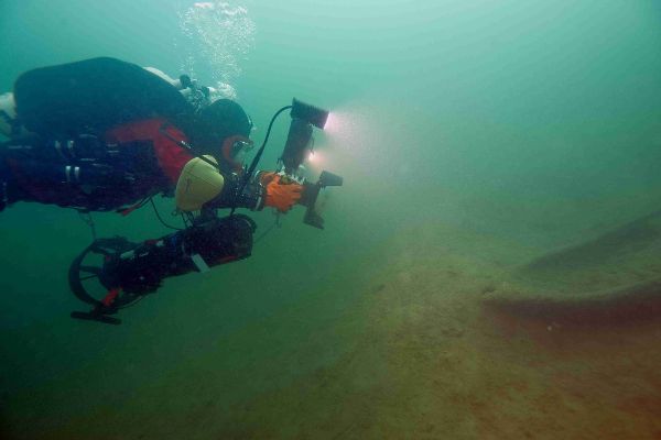 Unterwasserdokumentation eines Einbaums durch einen Taucher mittels Unterwasserkamera