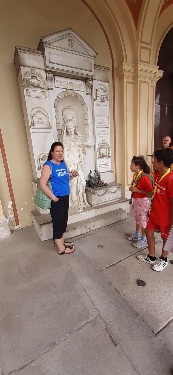 Eine Frau erklärt Kindern eine Steinfigur auf einem Grabmal