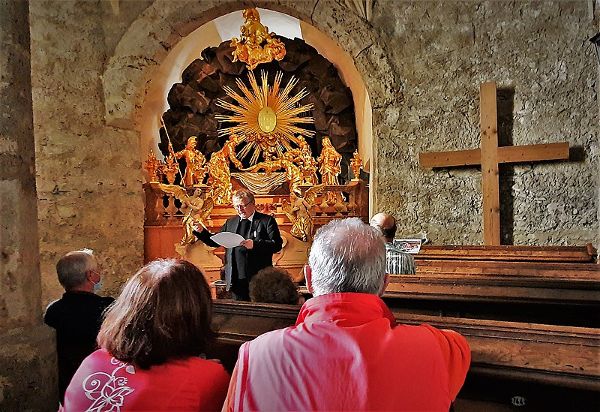 zwei Personen sitzen auf einer Kirchenbank, ein Priester predigt